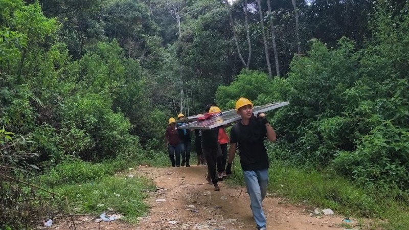 Dengan penuh semangat gotong royong, petugas PLN dan warga bahu-membahu memikul panel surya seberat hampir 100 kilogram menuju lokasi pemasangan di sekolah-sekolah.